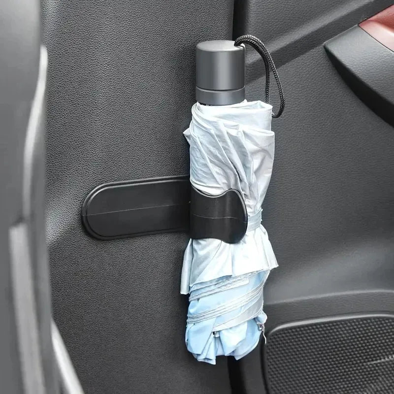 Car umbrella holder mounted on blue fabric near door handle. Secures 4PC universal fit. Functional add-on for rain protection