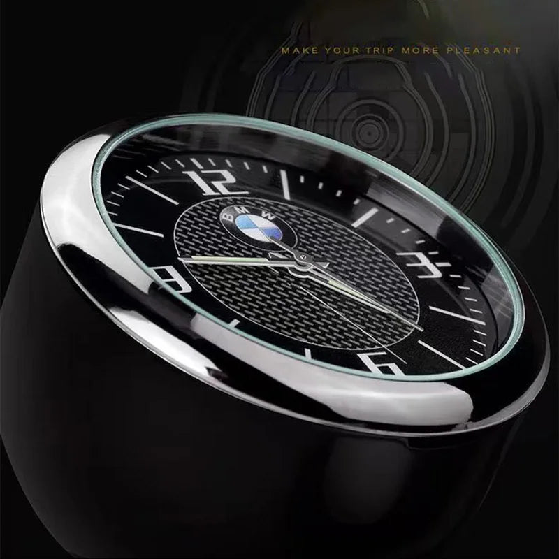 Black quartz clock with a matte black dial on BMW center console air conditioner vent mount.